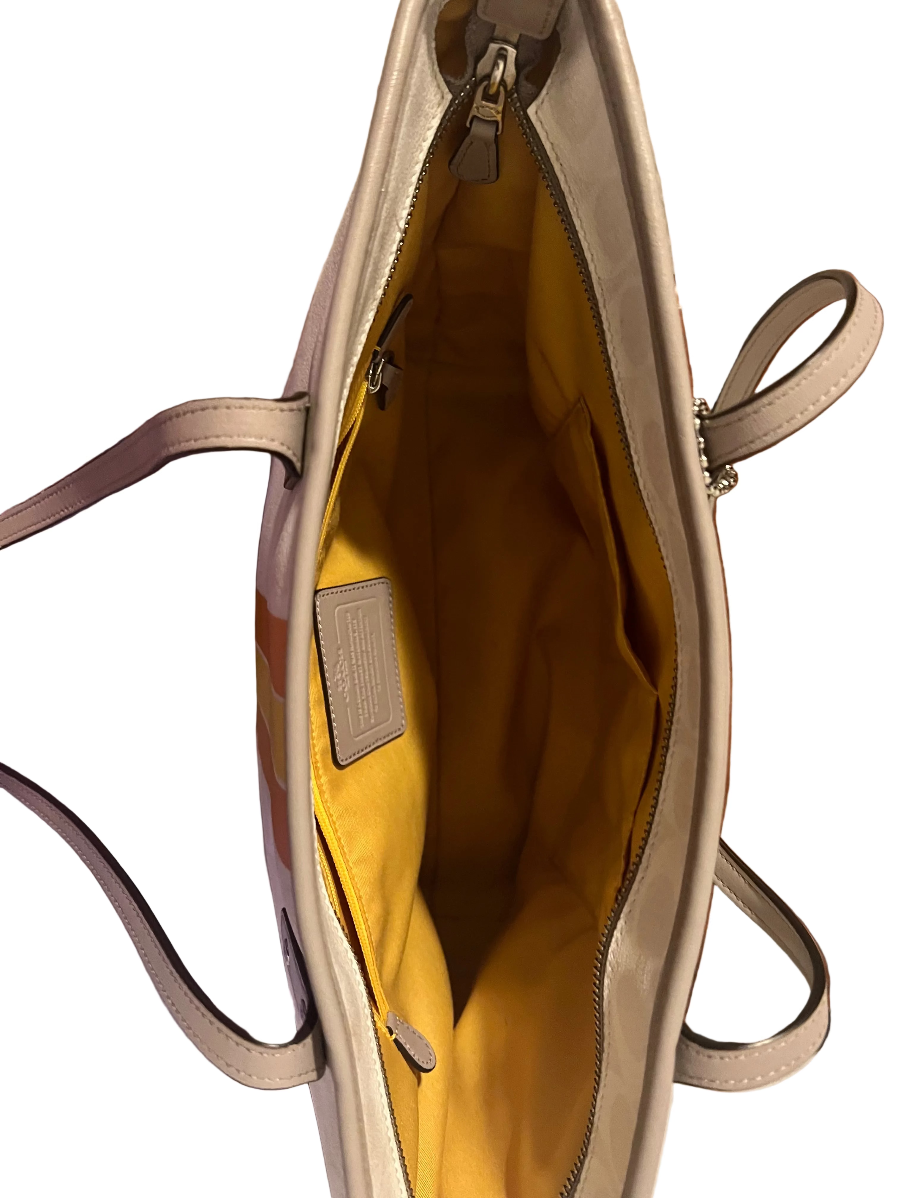 An open beige Coach tote bag with a bright yellow interior lining, shown from above. 