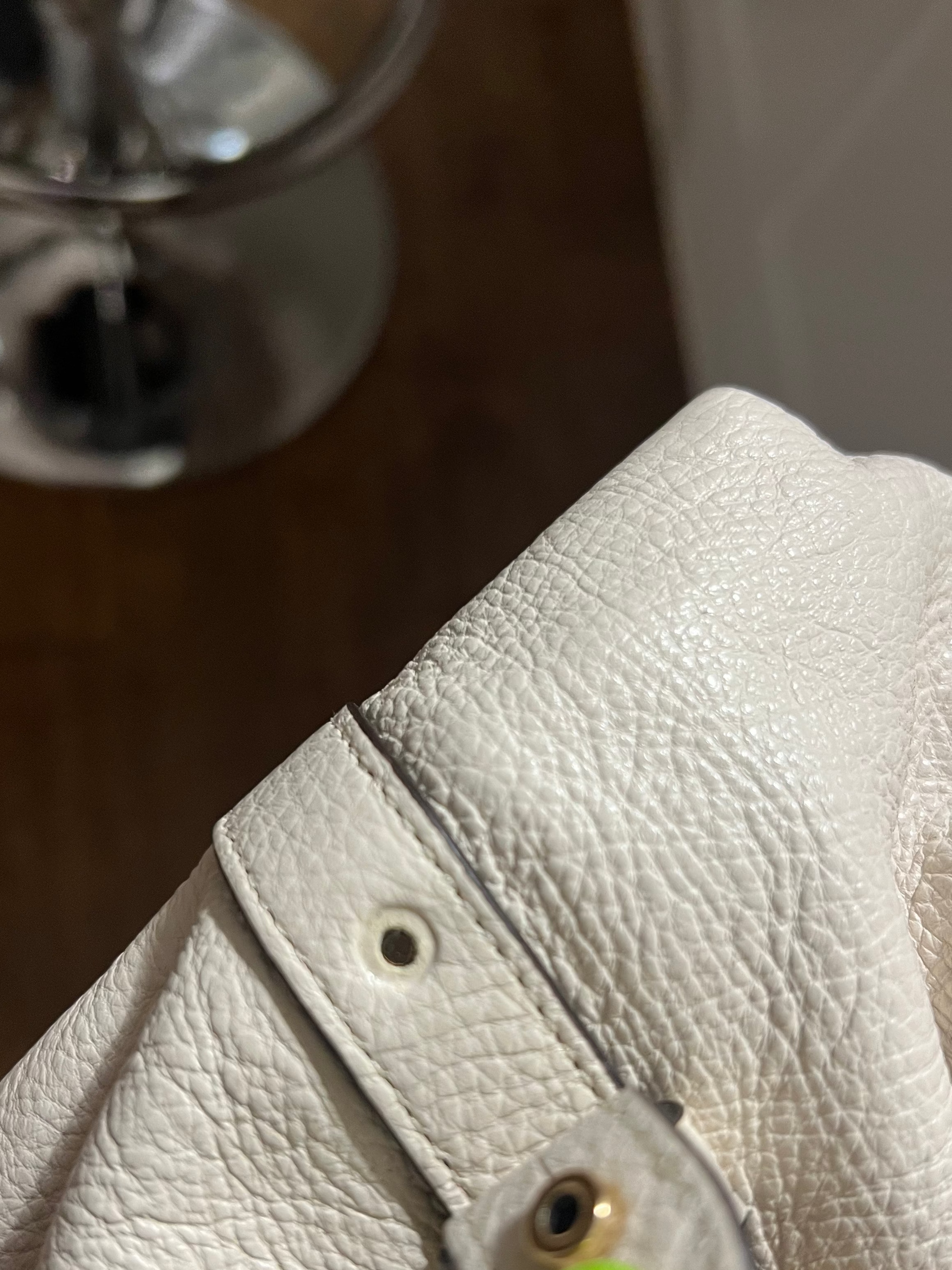 Close-up of a white pebbled leather handbag with a strap and gold-tone hardware